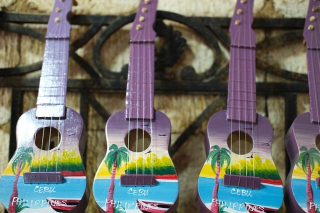 Three purple ukeleles painted with a beach scene hanging in a row.