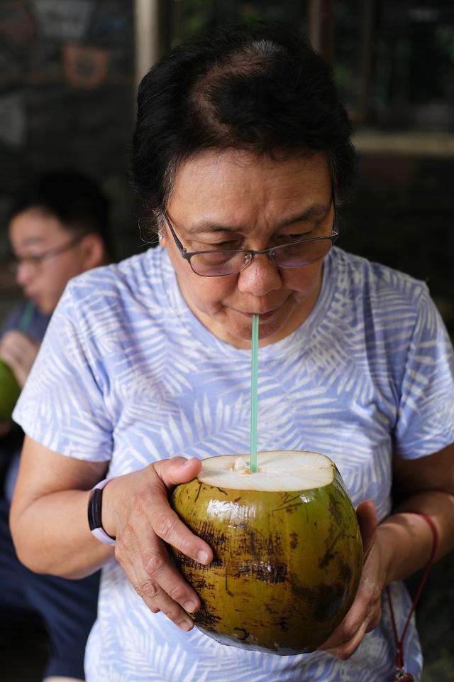 A woman sips buko juice directly from a young coconut using a straw.