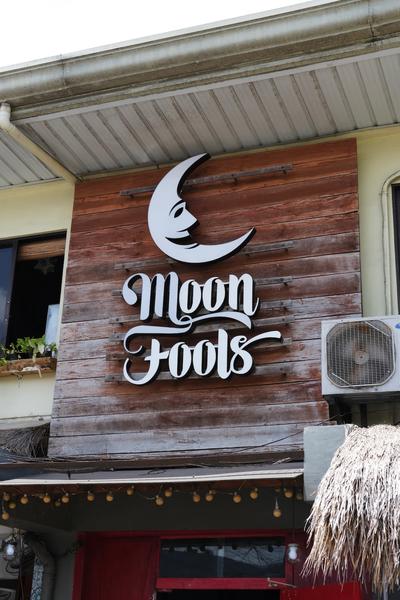 A sign with a quarter-moon face logo reading “Moon Fools”.