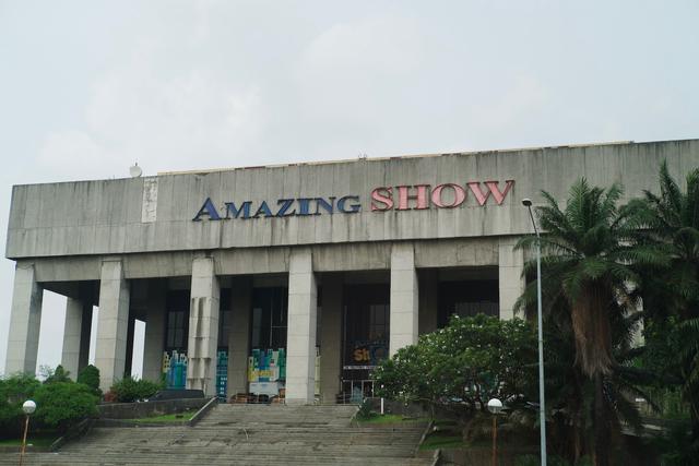 A weathered concrete theater with a facade that reads “Amazing Show”. The stairs leading up to the entrance are barred with chain-link fencing. An air of neglect hangs over the structure.