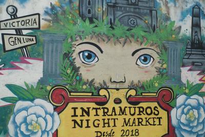 A mural containing a face framed by plants and columns, with a sign for Intramuros Night Market under the face.