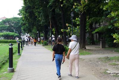 A girl in a black shirt and jeans carries a folding fan while walking next to an older woman in a blue straw hat.
