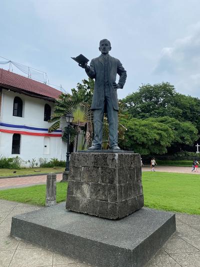 A metal statue of Jose Rizal atop a pedestal, looking out on a large courtyard.