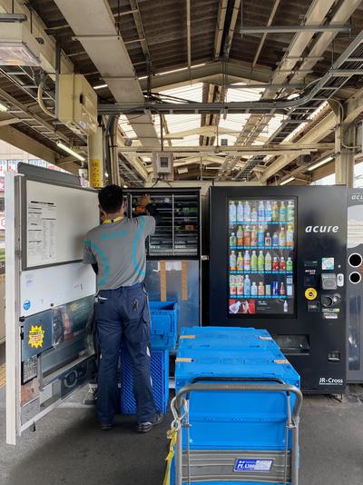 A man reloads a vending machine on a rail platform.