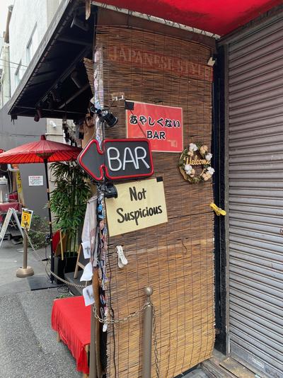 An entryway to a small bar, decorated with a woven bamboo covering. The sign says “Not Suspicious Bar”.