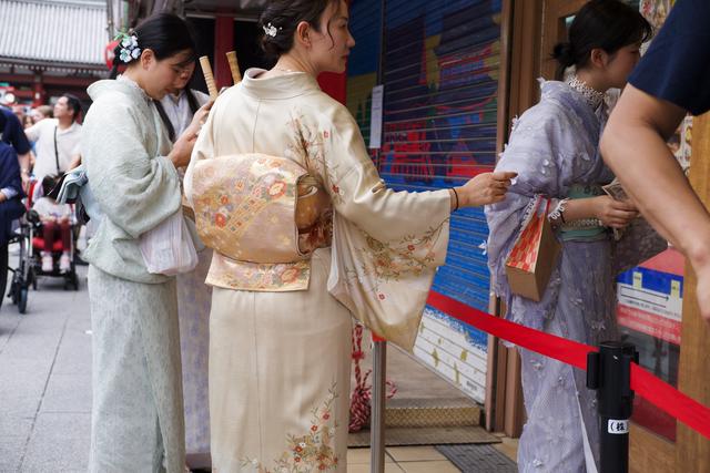 Women in ornate kimonos queue up in front of a shop along Nakamise Shopping Street.