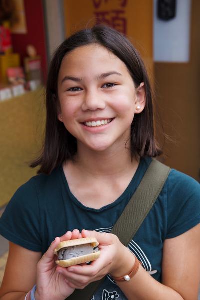 A girl in a green shirt holds up an ice cream sandwice.