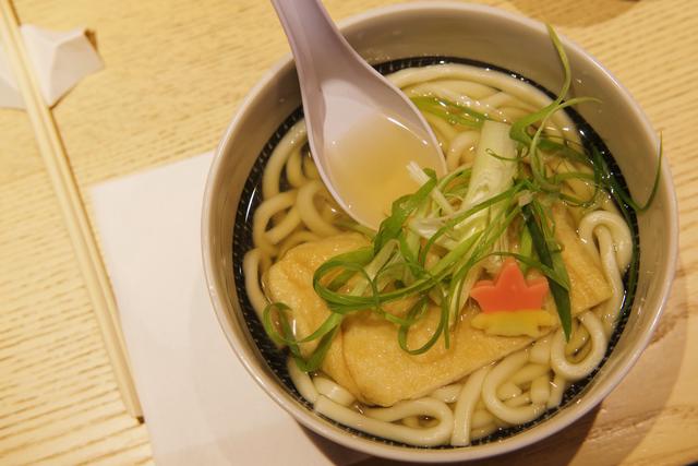 Closeup of a bowl of udon with tofu skin and shaved vegetable garnish.