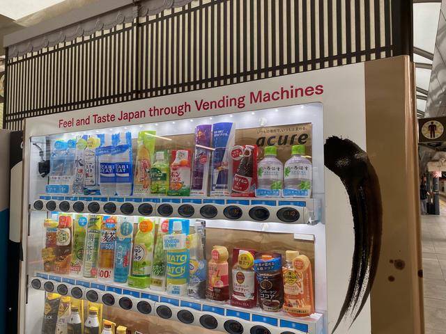 A vending machine on a rail platform. Across the top of the machine is the message, “Feel and Taste Japan Through Vending Machines”