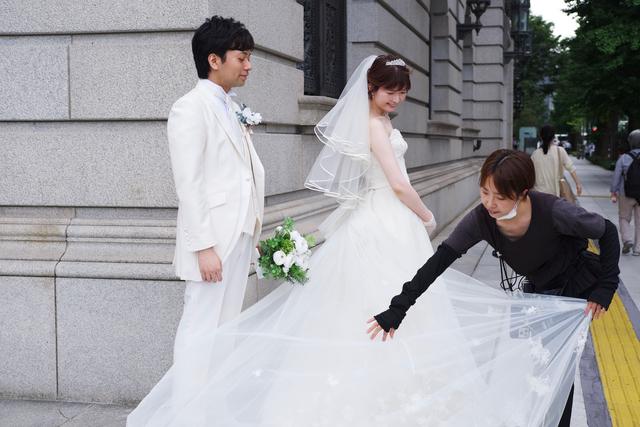 A man and a woman in wedding attire take photos on the street near Tokyo’s Imperial Palace. The photographer is arranging the woman’s dress.