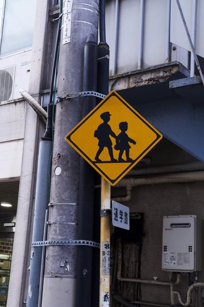 Yellow crossing sign with silhouttes of children in school clothes.