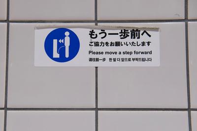 Signage in front of a urinal urging people to step closer.