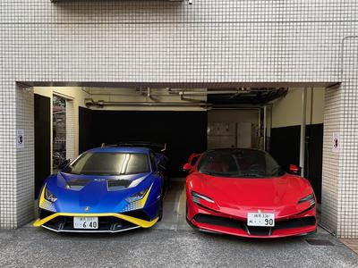 A pair of sports cars in a small garage: a blue one on the left, a red one on the right.