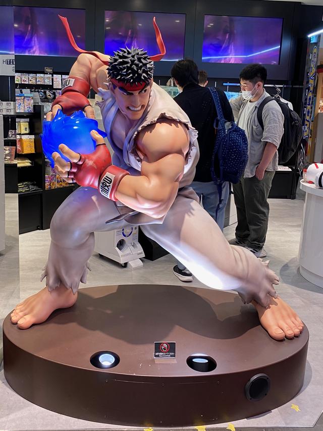 A giant figure of Ryu from the Street Fighter series. He is preparing to launch a fireball from his hands.