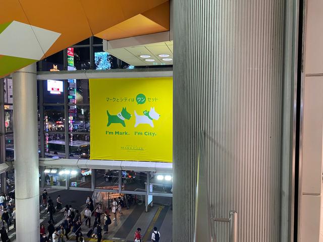 A billboard advertising the Shibuya Mark City store. Two illustrated silhouettes of dogs. Under the first dog it says “I’m Mark.”, under the other, “I’m City.”.