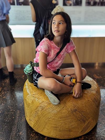 A girl sits on a seat sculpted to look like a large ball of uncooked ramen noodles.