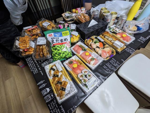 A dining table filled with packaged sushi, dumplings, and edamame.