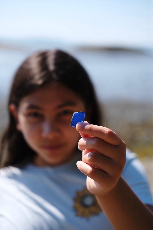 A girl holding up a piece of blue seaglass.