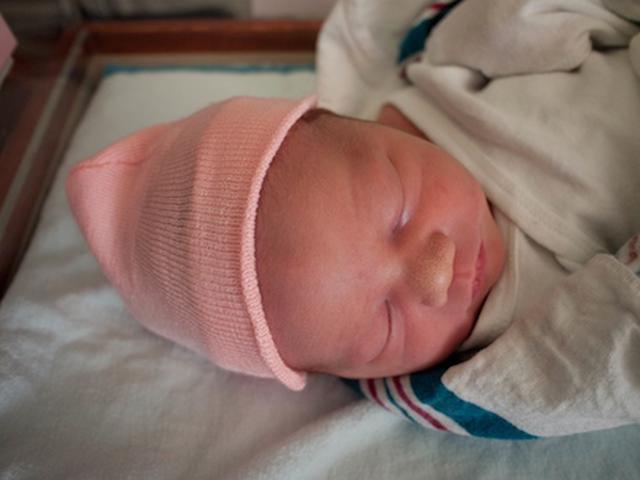 Newborn swaddled in a blanket with a pink hat