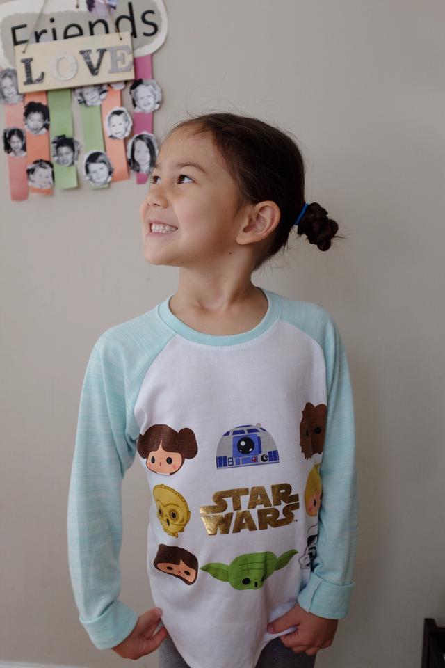 Young girl with a long-sleeved t-shirt featuring several Star Wars characters.