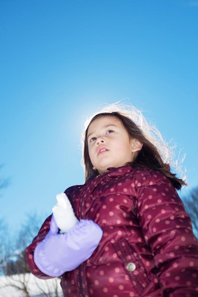 Girl in a winter coat, holding an icicle while lit up from behind by the sun.