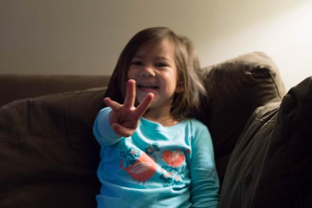 A smiling girl holds up three fingers