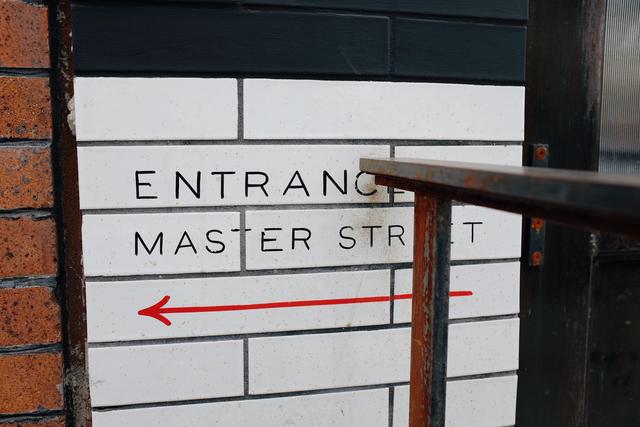 Left view of sign saying “Entrance via Master Street” cut off by hand rail