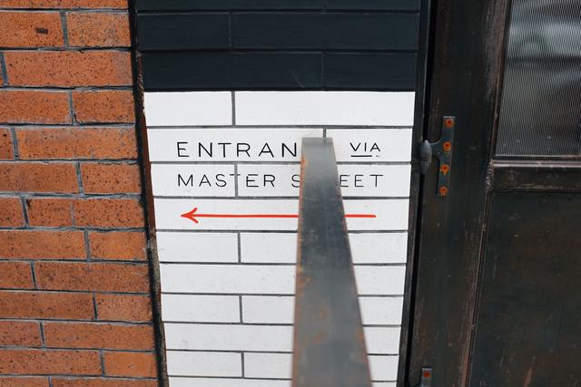 Center view of sign saying “Entrance via Master Street” cut off by hand rail